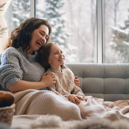 mother and daughter sit next to a window overlooking snowy scene